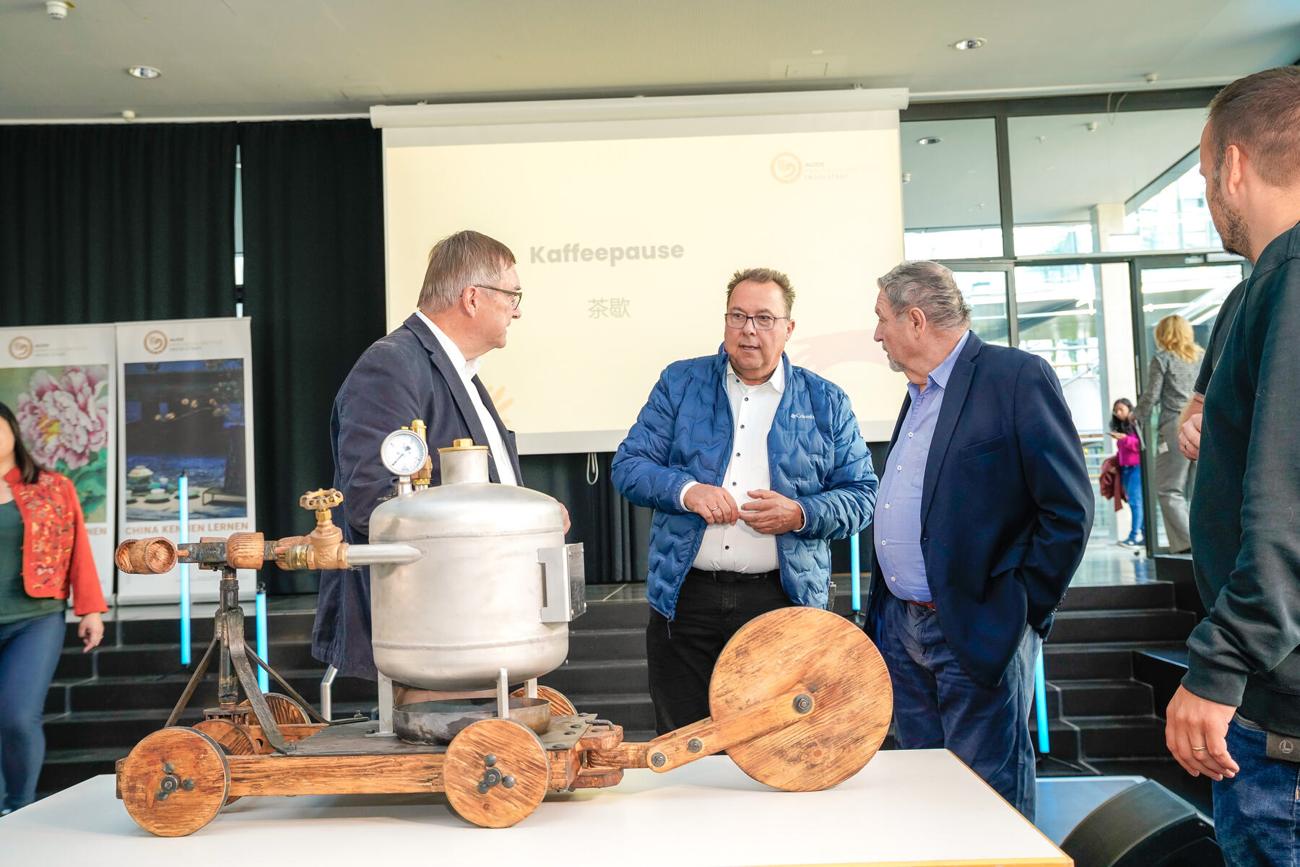 Gäste betrachten den Nachbau aus Edelstahlkessel und Holzrahmen