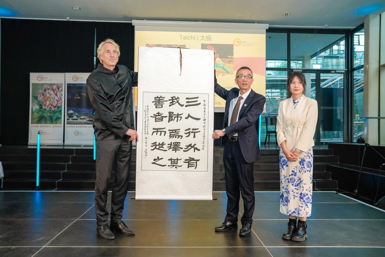Prof. Dr. Peter Augsdörfer und Prof. Dr. Bo Wu zeigen eine Kalligrafie mit dem Ausspruch 三人行必有我师
