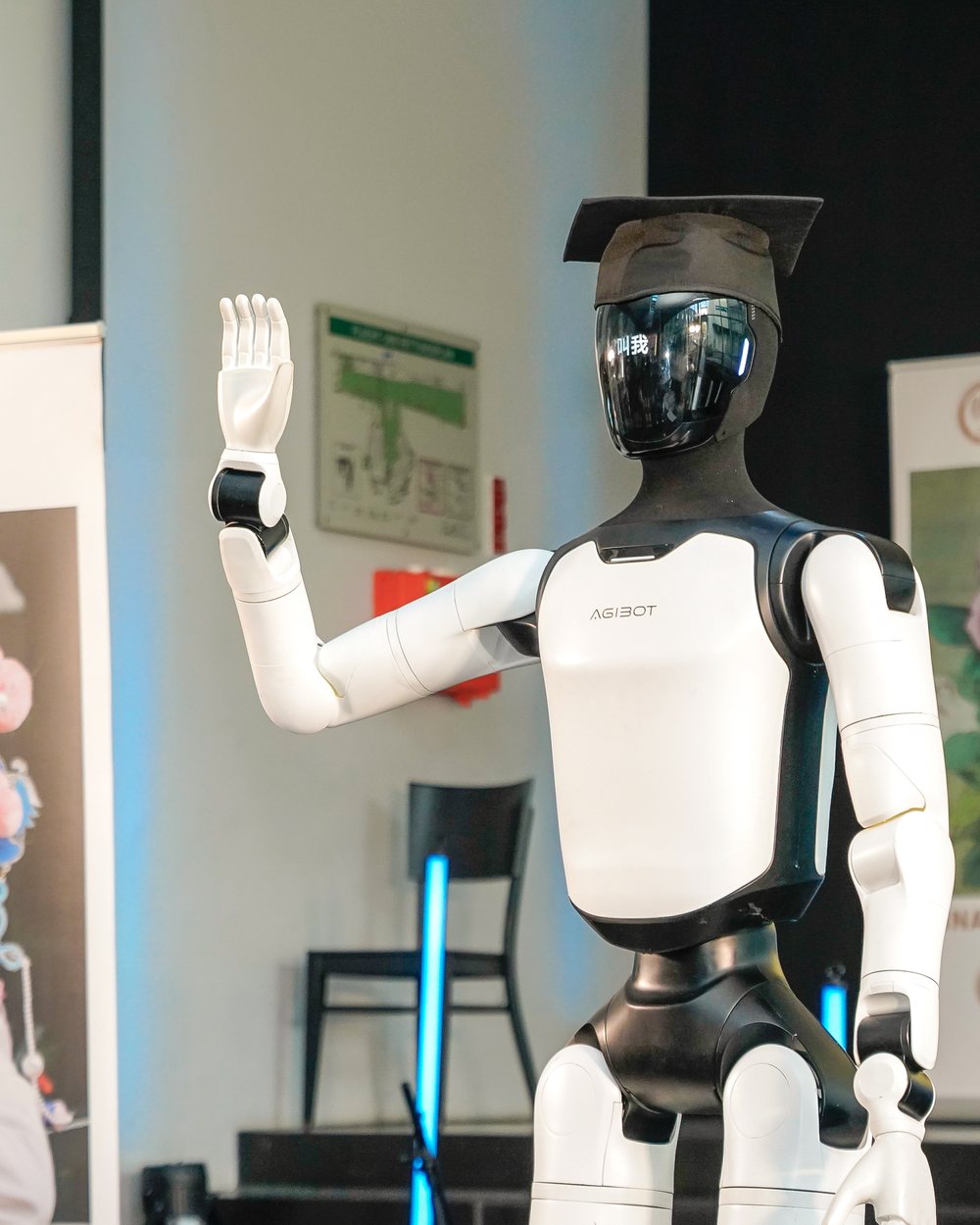 Roboter Luca winkt auf der Bühne, auf dem Kopf ein Doktorhut